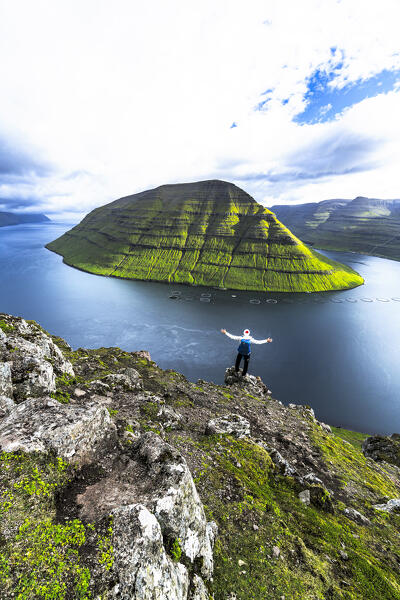 Cheerful man with arms outstretched admiring the fjord standing on mountain top, Klaksvik, Bordoy Island, Faroe Islands