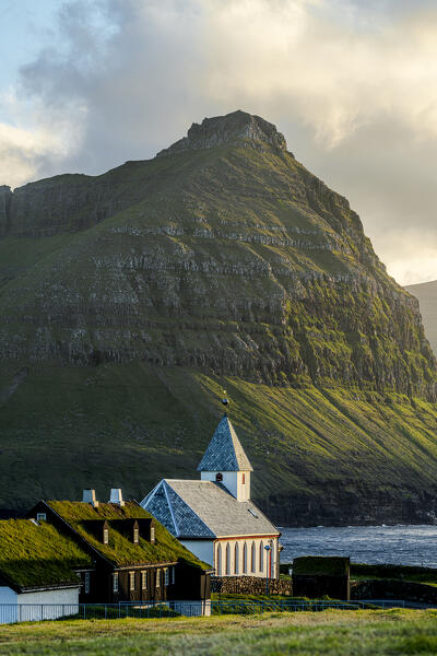 Vidareidi church and grass roof houses framed by  majestic mountains of Bordoy island, Vidoy Island, Faroe Islands