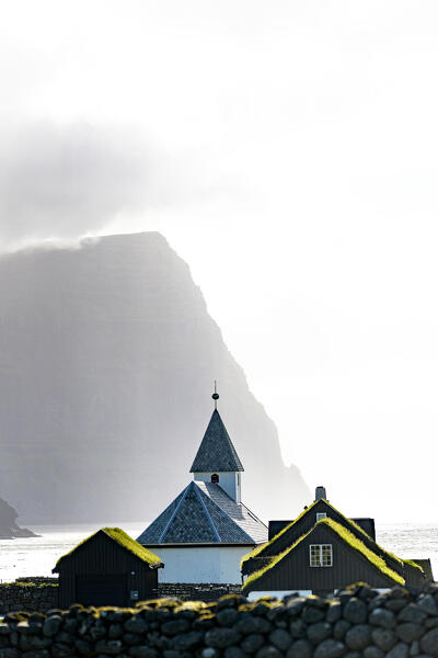 Misty sky over the traditional church of Vidareidi ovelooking a fjord, Vidoy Island, Faroe Islands