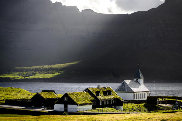 Sunlight over the traditional grass roof houses and old church, Vidareidi, Vidoy Island, Faroe Islands