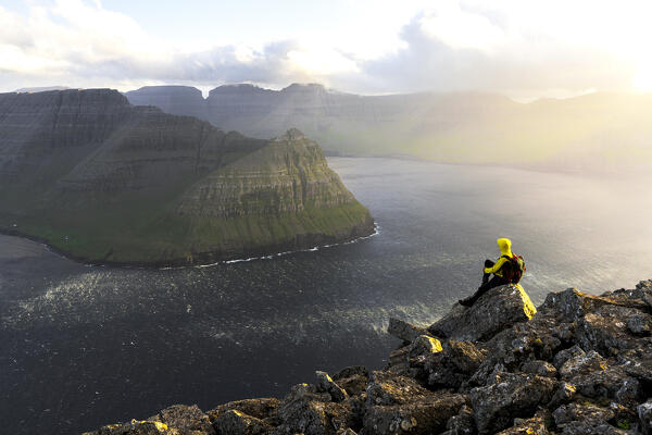 Hiker with backpack admiring the fjord standing on mountain peak in summer, Vidareidi, Vidoy Island, Faroe Islands