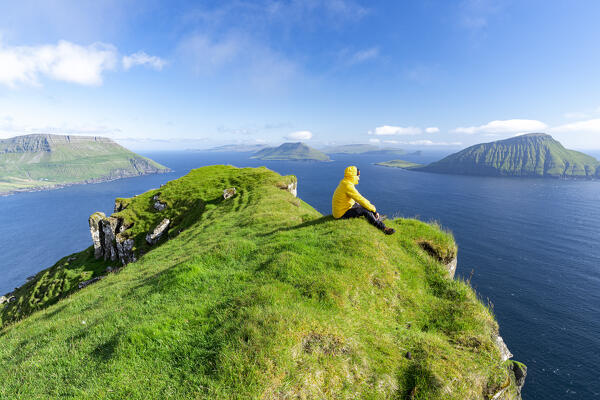 Man relaxing on grass on top of cliffs overlooking the ocean, Nordradalur, Streymoy Island, Faroe Islands (MR)