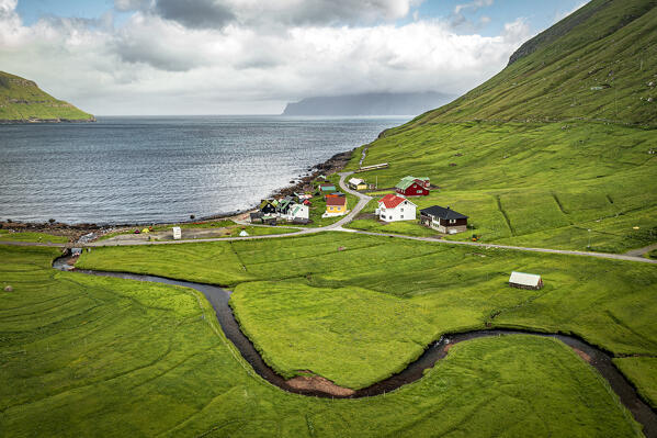 Aerial view of river crossing the green fields towards the coastal village of Elduvik, Eysturoy Island, Faroe Islands