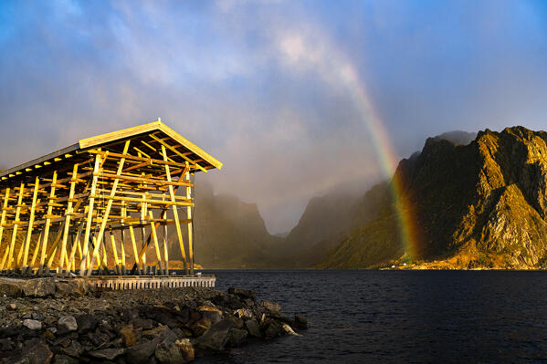 Colorful rainbow over mountains and fishing racks overlooking the cold sea, Sakrisoy, Reine, Lofoten Islands, Norway