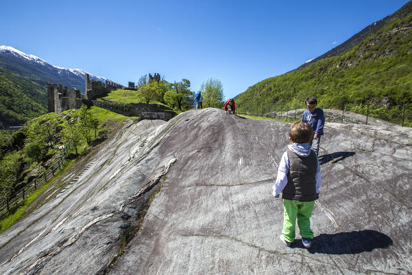 Children searching rock engravings on huge Rupe Magna. Grosio. Province of Sondrio. Valtellina. Lombardy. Italy. Europe