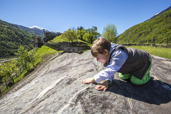 Child observes petroglyphs of Rupe Magna near the Castle Visconti Venosta in Grosio. Province of Sondrio. Valtellina. Lombardy. Italy. Europe