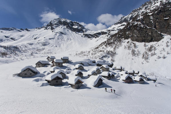 Hikers with snowshoes to submerged snow huts of Lendine Alp. In the background the Pizzaccio. Valchiavenna. Valtellina. Lombardy. Italy. Europe. 