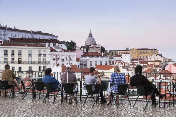 Tourists admire terracotta roofs and ancient dome from a terrace at Miradouro Alfama viewpoint of Lisbon Portugal Europe