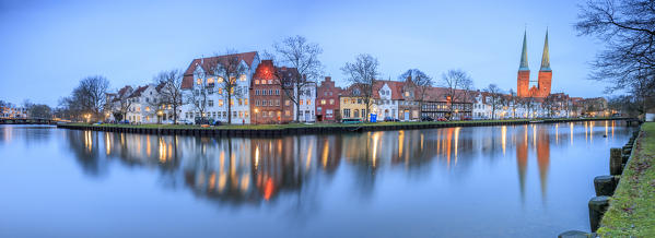 Panorama of typical houses and towers of cathedral reflected in river Trave at dusk Lübeck Schleswig Holstein Germany Europe