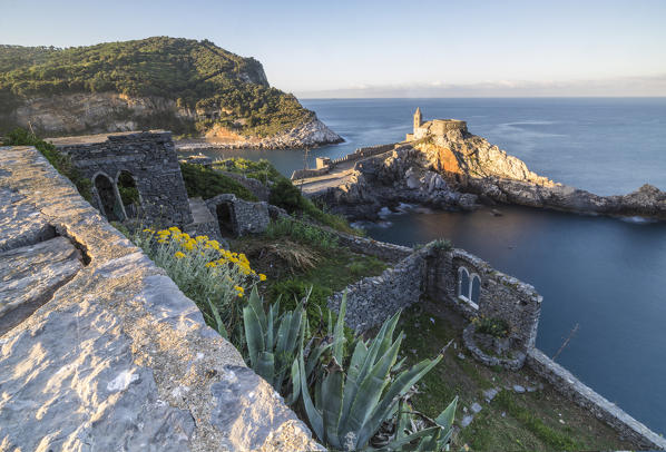 Flowers and blue sea frame the old castle and church at dawn Portovenere province of La Spezia Liguria Italy Europe