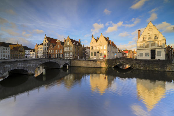 First lights of sunrise on the historic buildings and bridges reflected in the typical canal Bruges West Flanders Belgium Europe