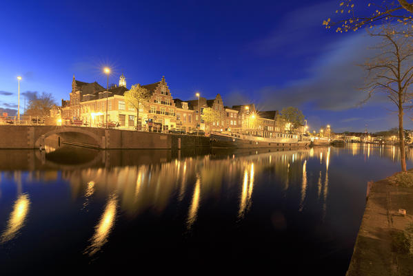 Dusk lights up the typical houses and bridge reflected in a canal of river Spaarne Haarlem North Holland The Netherlands Europe