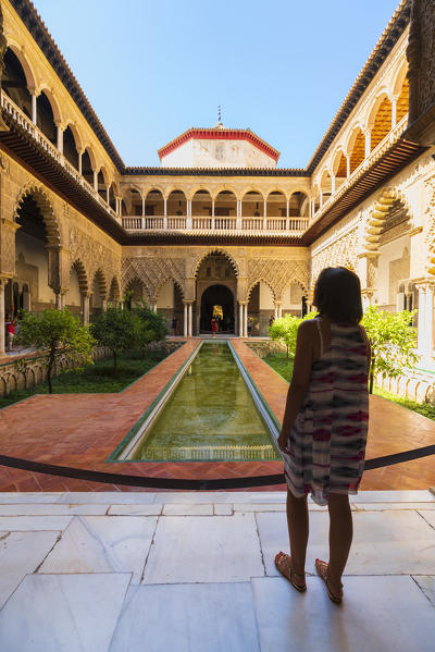 Woman admiring the Patio de las Doncellas, a decorated courtyard and pool in typical Mudejar architecteure. Real Alcazar, Seville, Andalusia, Spain