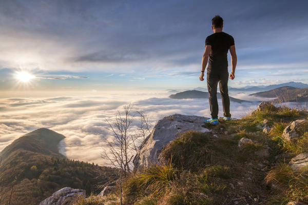 Hiker admire the panorama and clouds under him on the top of Bronzone Mount (Prealpi Orobiche). Viadanica, Bergamo province, Lombardy, Italy, Europe