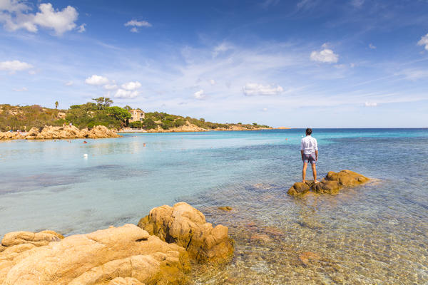A young man admiring the view standing on rocks in Capriccioli beach, Arzachena Costa Smeralda, Olbia-Tempio province, Sardinia district, Italy