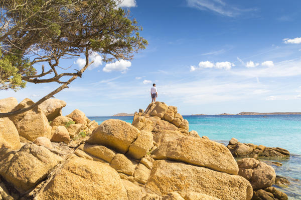 A young man admiring the view standing on rocks in Capriccioli beach, Arzachena Costa Smeralda, Olbia-Tempio province, Sardinia district, Italy