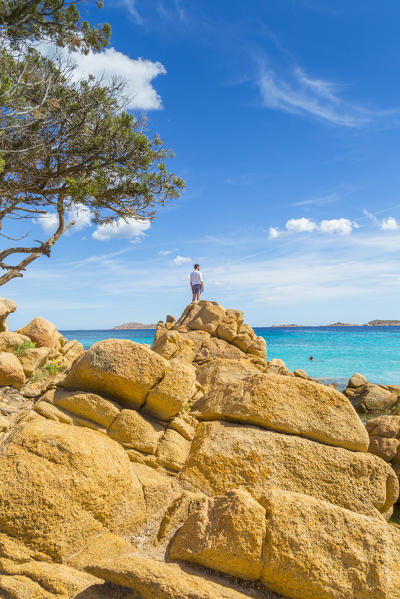 A young man admiring the view standing on rocks in Capriccioli beach, Arzachena Costa Smeralda, Olbia-Tempio province, Sardinia district, Italy