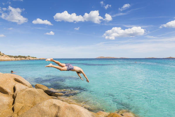 A young man jumping off cliff into the sea in Capriccioli beach, Arzachena Costa Smeralda, Olbia-Tempio province, Sardinia district, Italy