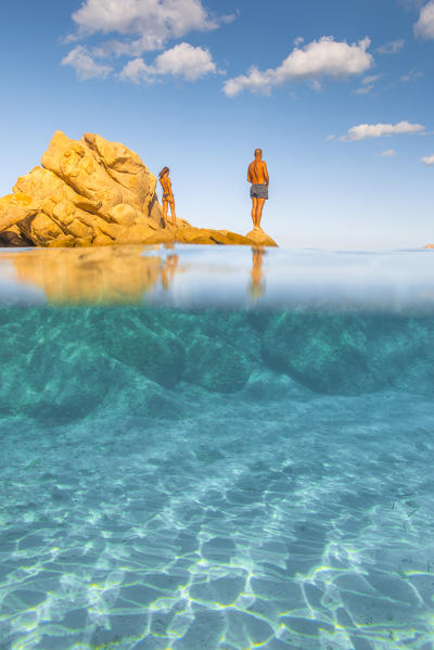 A couple relaxing admiring the view and the crystal turquoise water standing on rocks in Capriccioli beach, Arzachena Costa Smeralda, Olbia-Tempio province, Sardinia district, Italy