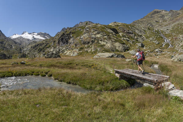 Hiker through the bridge on the path leading to the Testa del Rutor, Valgrisenche, Aosta Valley, Italy