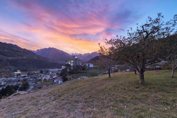 Colorful sunset among the apple orchard overlooking the Castle of Saint-Pierre, Aosta Valley, Italy
