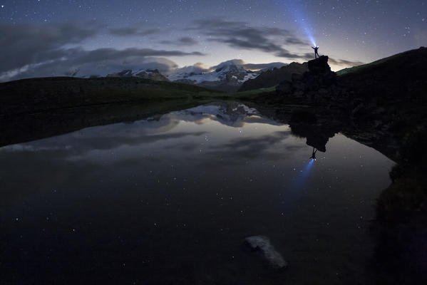 Hiker with the torch reflected in the small lake of Pian Borgno, Valsavarenche, Aosta Valley, Italy