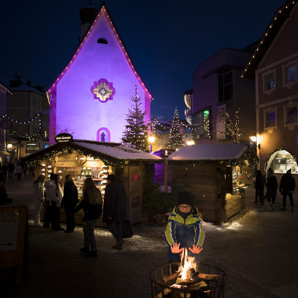 a child is warming in front of a bonfire by the Christmas market in Val Gardena, Bolzano province, South Tyrol, Trentino Alto Adige, Italy