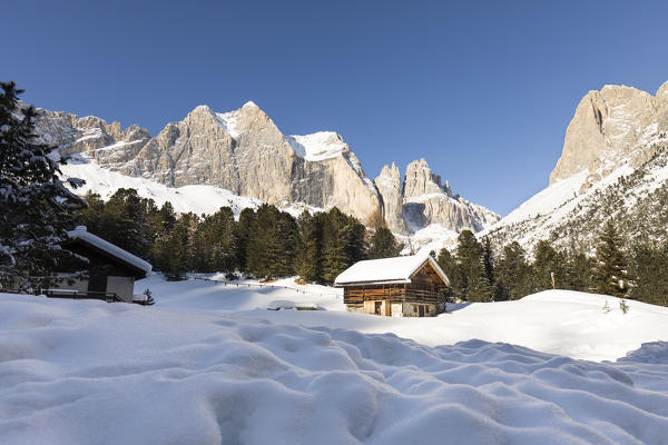 a winter landscape in Fassa Valley with the Rosengarten in the background and two little huts in the foreground, Trento province, Trentino Alto Adige, Italy