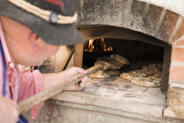 a baker checks the cooking of the bread into the oven, bolzano province;italy;south tyrol;trentino alto adige