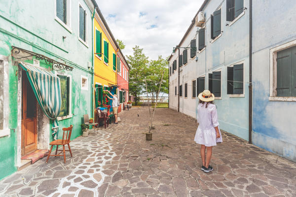 A woman in the middle of rows of colorful buildings in Burano, Venice, Veneto, Italy, Europe