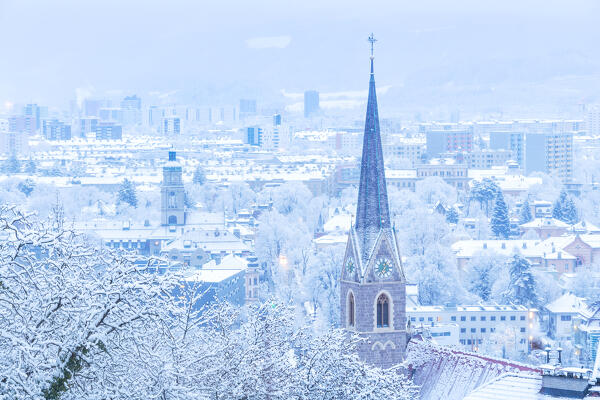 The bell tower of Sankt Nikolaus with the snow-covered city of Innsbruck in the background, Innsbruck , Tyrol, Austria, Europe