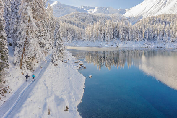Aerial view of two hikers and a dog walking around Lake Obernberg after a heavy snowfall, Obernberg am Brenner, Innsbruck Land, Tyrol, Austria, Europe 