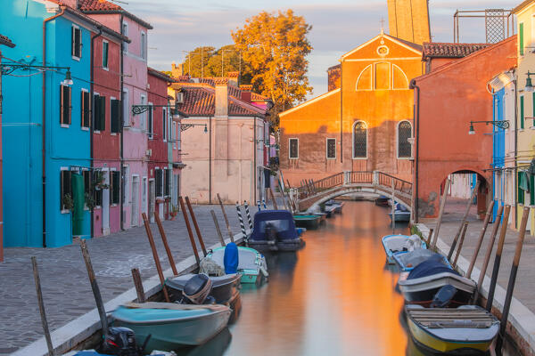 A row of boats leading to the Terranova's marble bridge with the San Martino church in the background at dawn, Burano, Venice, Veneto, Italy, Europe