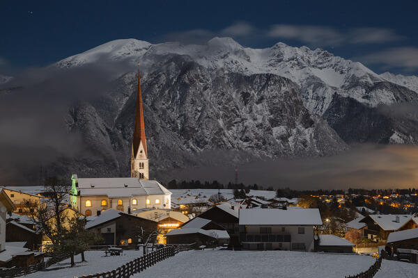The parish church St. John the Baptist and St. John the Evangelist with the Karwendel mountains illuminated by the moonlight on a winter night, Axams, Westliches Mittelgebirge, Innsbruck Land, Tyrol, Austria, Europe
