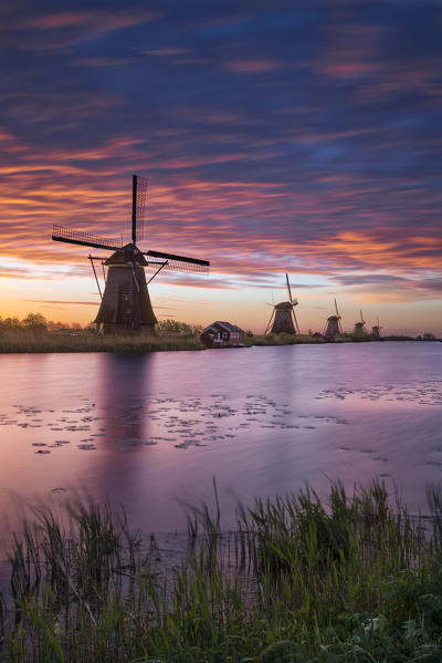 The windmills of Kinderdijk during the dawn with red/orange clouds (Molenwaard municipality, South Holland, Netherlands) 
