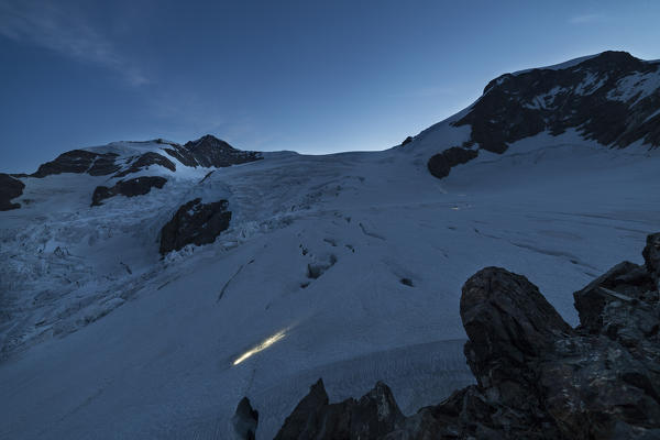 Mountaineers start to walk at dawn on Lys glacier near the Gnifetti refuge in Monte Rosa Massif (Gressoney, Lys Valley; Aosta province, Aosta Valley, Italy, Europe)