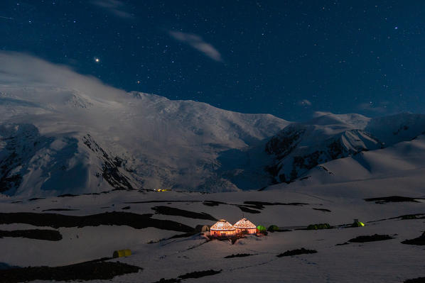 Nightscape of peak Lenin camp one with Peak Lenin massif in the background under a starring sky. Pamir, Kyrgyzstan, Central Asia. 