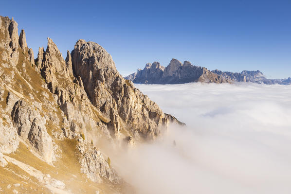 Latemar mount rocks over a cloudy carpet with Catinaccio group in background. Latemar group, Costalunga pass, Fassa valley, Pozza di Fassa, Trento district, Dolomites, Italy, Europe.