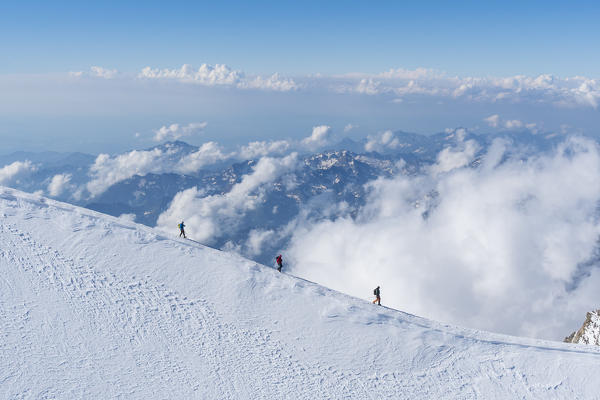 Alpinists along a snow ridge in Rosa group with clouds and mountain profiles in the background. Gressoney, Aosta district, Valle d'Aosta, Alps, Italy, Europe. 