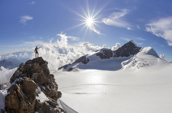 Alpinist over a rock near Balmenhorn bivac looking to Lyskamm peak with sun in backlight. Gressoney, Aosta district, Valle d'Aosta, Alps, Italy, Europe. 