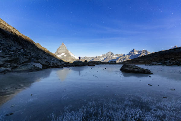 One tourist looks Matterhorn at Riffelsee, during a full moon night. Zermatt, Mattertal, Canton of Valais, Switzerland, Europe