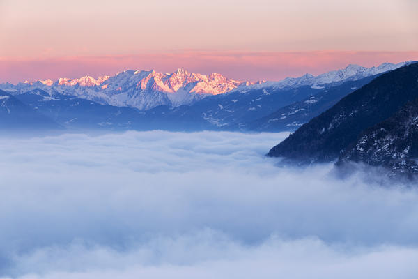 Sea of fog in Valtellina with Adamello group in the background at sunset. Valtellina, Lombardy, Italy, Europe.