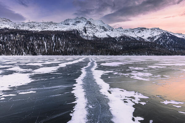Colors of sunset is reflected on the frozen surface of Lej da Silvaplana. Engadine Valley, Graubunden Canton, Switzerland, Europe