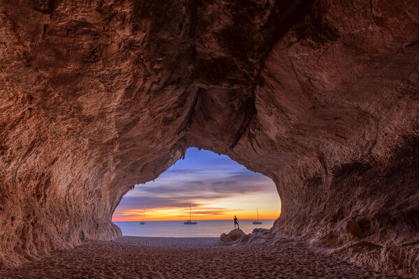Lonely person looks colors of the sunrise inside the sea cave on the beach of Cala Luna, Baunei, Ogliastra province,  Sardinia, Italy, Europe