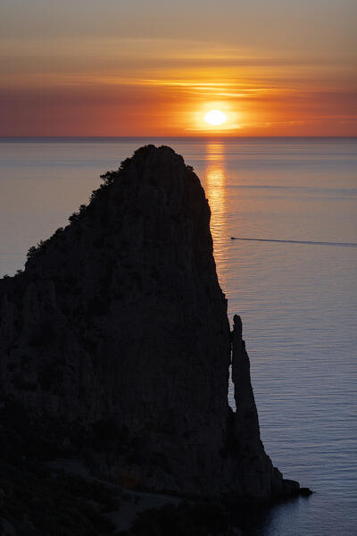 The sun is reflected on the sea surface at sunrise with Pedra Longa monolith in silhouette. Baunei, Ogliastra province, Sardinia, Italy, Europe
