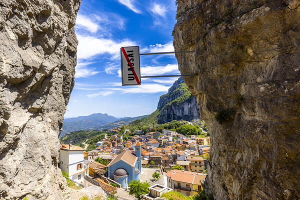 Crooked road sign(Art installation) with view of Ulassai village between two rock walls. Nuoro Province, Sardinia, Italy, Europe