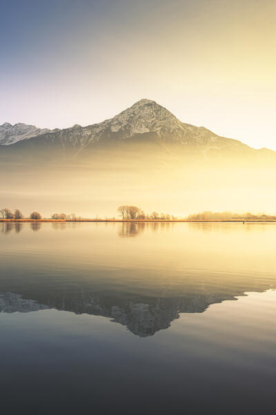 Foggy sunset light on the Mezzola lake with Monte Legnone is reflected in the water, Lombardy, Italy, Europe.