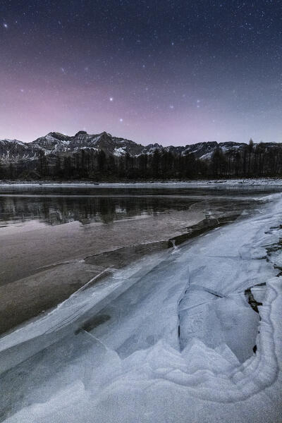 Night view of the frozen Lagazzuolo lake with northern light in the sky.  Valtellina,Valmalenco, Lombardy, Italy, Europe.
