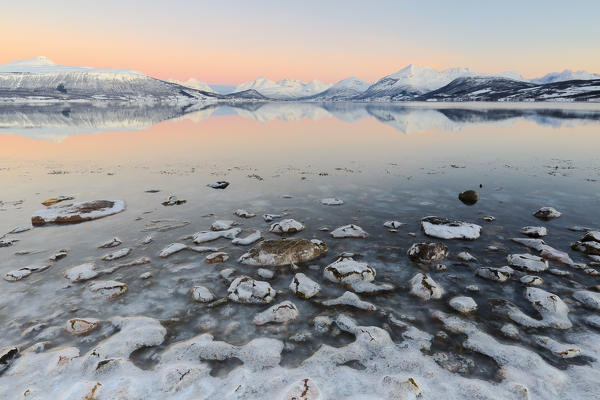 Cloudless sunrise with ice covering the stones on the shore of Balsfjorden. Markenes, Balsfjorden, Lyngen Alps, Troms, Norway, Lapland, Europe.