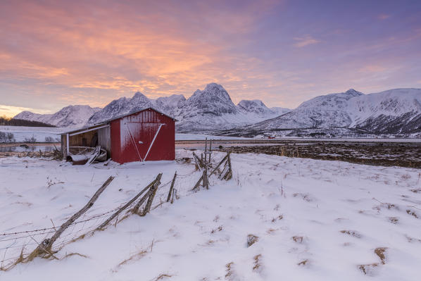 Red house of fishermans at sunrise on the beach. Storsteinnes, Balsfjorden, Lyngen Alps, Troms, Norway, Lapland, Europe.